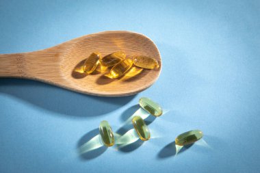 Mavi arka planda balık yağı Omega 3 kapsülleri.