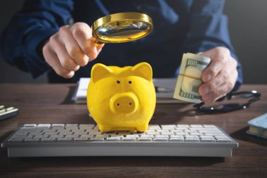 Businessman holding magnifying glass over piggy bank and dollar banknotes. clipart