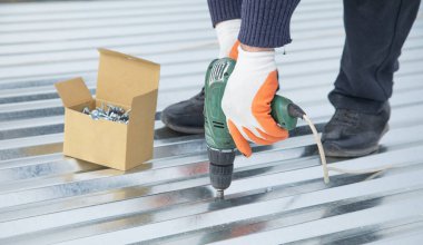 Elektrikli sondaj makinesiyle metal çatı döşeyen adam.