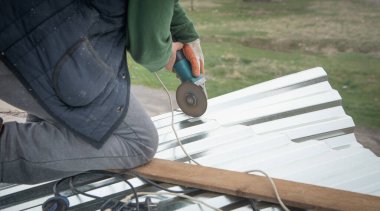 İşçi evin çatısına yerleştirmek için metal bir levha kesiyor.. 