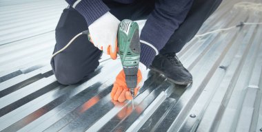 Elektrikli sondaj makinesiyle metal çatı döşeyen adam.