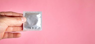 Erkek el pembe arka planda prezervatif gösteriyor..