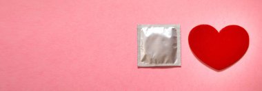 Pembe arka planda prezervatif ve kırmızı kalp.. 