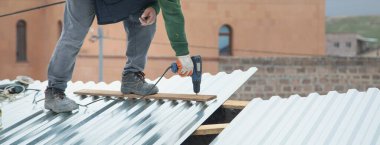 Elektrikli sondaj makinesiyle metal çatı döşeyen adam.