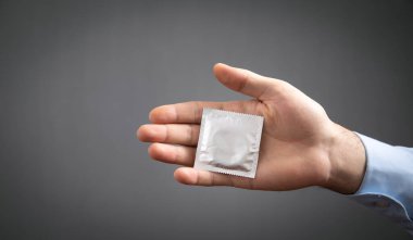 Erkek el, gri arka planda prezervatif gösteriyor..