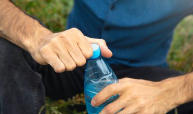 Adam dışarıda maden suyu şişesini açıyor..