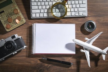 Hesap makinesi, not defteri, madeni paralar, retro kamera, ahşap arka planda uçak..