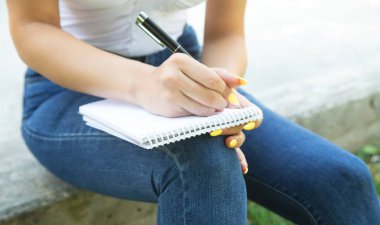 Açık havada not defterine kalem yazan bir kadın..