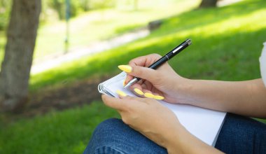 Açık havada not defterine kalem yazan bir kadın..