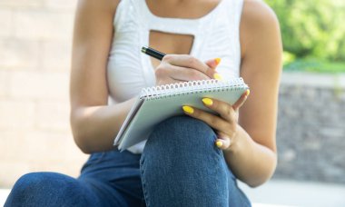 Açık havada not defterine kalem yazan bir kadın..