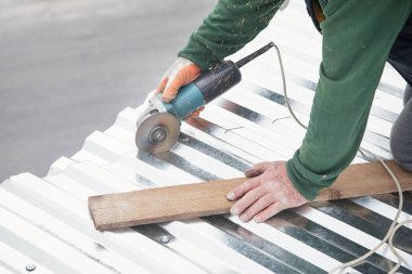 İşçi evin çatısına yerleştirmek için metal bir levha kesiyor.. 