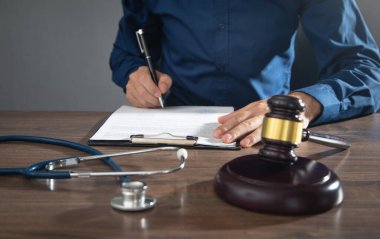 Belge imzalayan adam. Yargıç Tokmak ve steteskop masada.