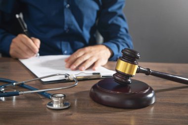 Belge imzalayan adam. Yargıç Tokmak ve steteskop masada.