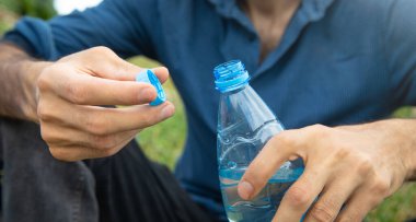 Adam dışarıda maden suyu şişesini açıyor..