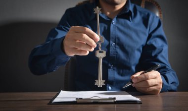 Anahtarları tutan ve kontratı imzalayan adam.