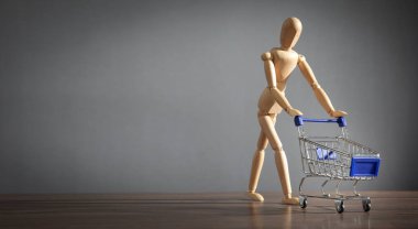Alışveriş arabası ve dizüstü bilgisayarı olan tahta insan figürü..