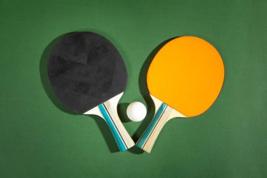 Masa tenisi raketleri ve yeşil arka planda beyaz plastik bir top..