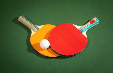 Masa tenisi raketleri ve yeşil arka planda beyaz plastik bir top..