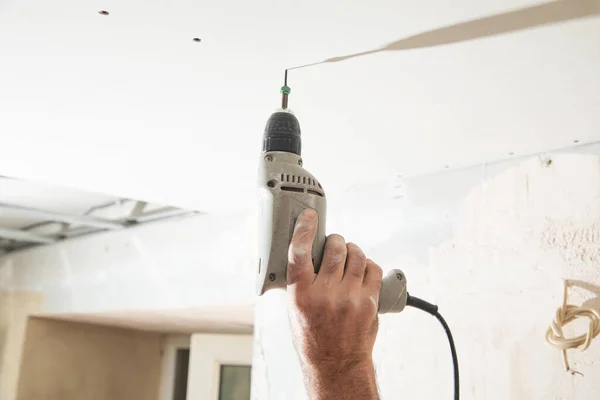 Worker with a drill screwdriver twists the screw into the drywall.