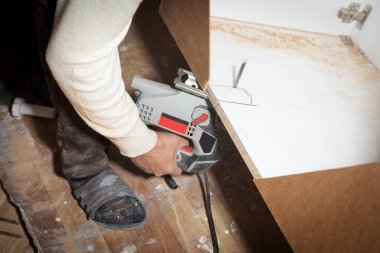 Elektrikli testere kullanarak mutfak dolabını kesen bir işçi..