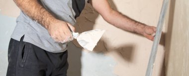 Adam duvara macun yapıştırıyor. Ev yenileniyor. 