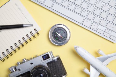 Eski kamera, not defteri, oyuncak uçak ve sarı arka planda pusula..