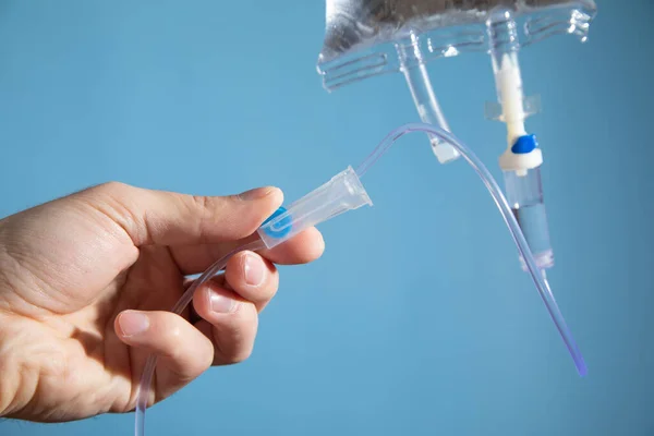 Male hand checking an intravenous drip on the blue background.