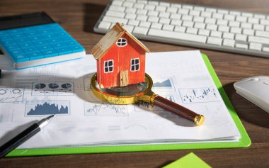 Ev modeli, grafikler, masada iş objeleri olan büyüteç..