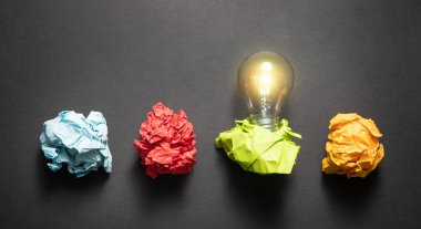 Siyah arkaplanda renkli kağıt toplar ve ampul.