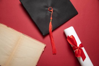 Bordeaux arka planında mezuniyet şapkası ve diploması..