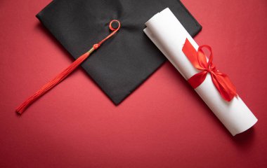 Bordeaux arka planında mezuniyet şapkası ve diploması..