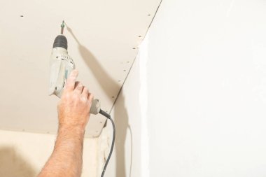 Matkap tornavidalı bir işçi vidayı alçıpana çeviriyor..