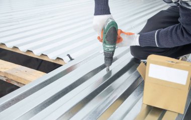 Elektrikli sondaj makinesiyle metal çatı döşeyen adam.