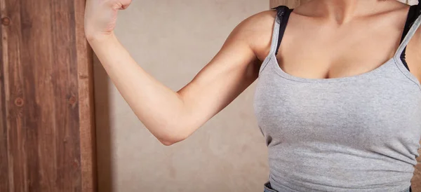 Young woman showing her biceps at home.