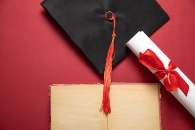 Bordeaux arka planında mezuniyet şapkası ve diploması..