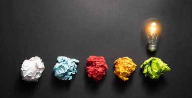 Siyah arkaplanda renkli kağıt toplar ve ampul.