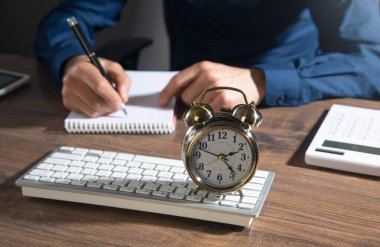 Ofiste çalışan bir iş adamı ve masada çalar saati var..