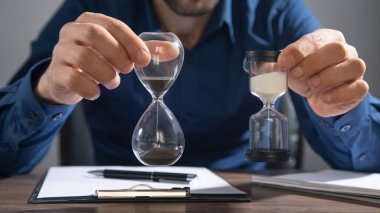 İş adamı masada kum saati tutuyor..