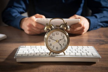 Ofiste çalışan bir iş adamı ve masada çalar saati var..