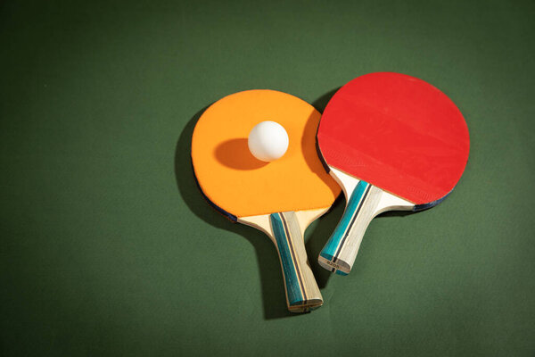 Table tennis rackets and a white plastic ball on the green background.