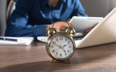 Ofiste çalışan bir iş adamı ve masada çalar saati var..