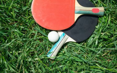 Masa tenisi raketleri ve yeşil çimlerin üzerinde beyaz plastik bir top..