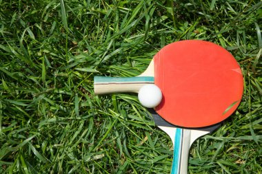 Masa tenisi raketleri ve yeşil çimlerin üzerinde beyaz plastik bir top..