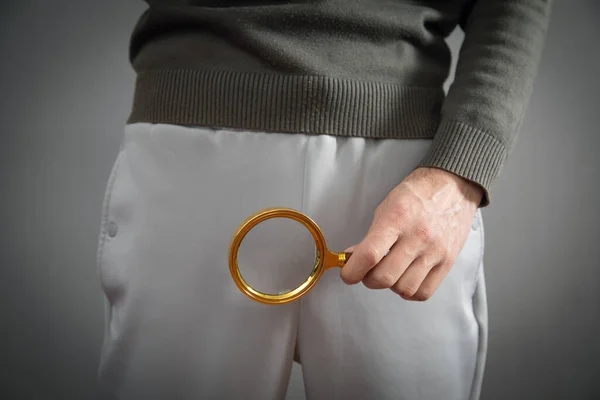 Man with a magnifying glass looking his penis.