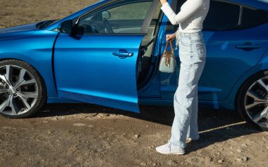 Arabanın yanında çantalı bir kadın var..