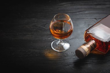 Koyu arkaplanda bir bardak konyak ve şişe..