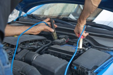 Arabayı şarj etmek için pil kablosu tutan adam..