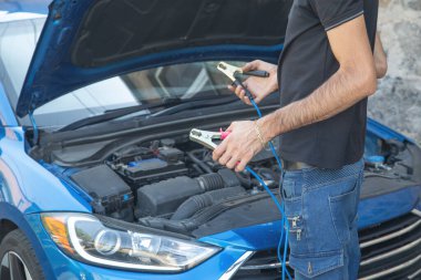 Arabayı şarj etmek için pil kablosu tutan adam..