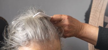 Yaşlı kadın saçlarını tarayan bir kadın el.