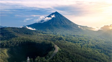 Endonezya 'nın Endonezya Dağı' nın altın saatindeki çarpıcı dikey çekimi. Zirvesinde bulutlar olan volkan kuleleri, yemyeşil bir krater nefes kesen manzarayı güçlendirirken,.